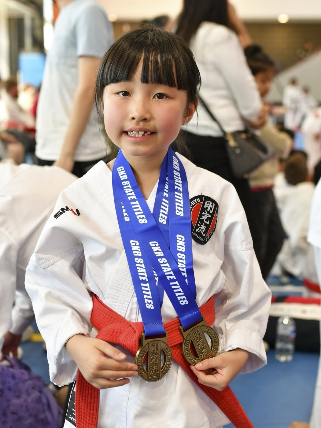 A young red-belt competitor smiling with two GKR State Titles medals around her neck.