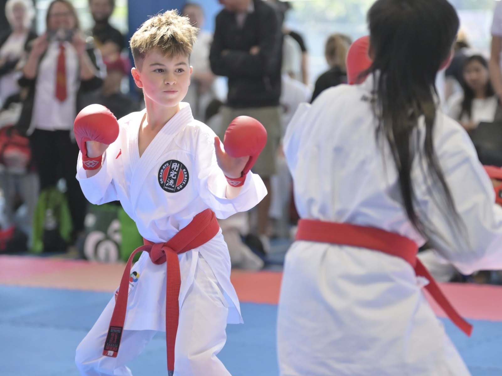 A young red-belt competitor with gloves up in fighting stance, focused on his opponent.