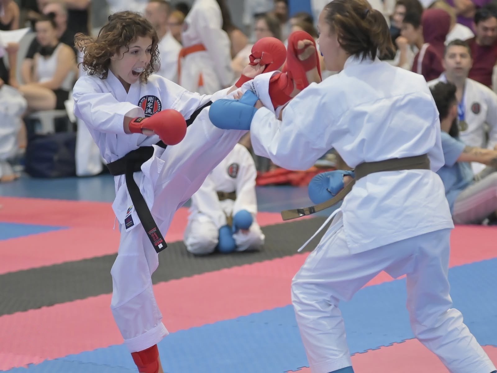 A junior black belt landing a front kick on an opponent's gloves during a kumite bout.
