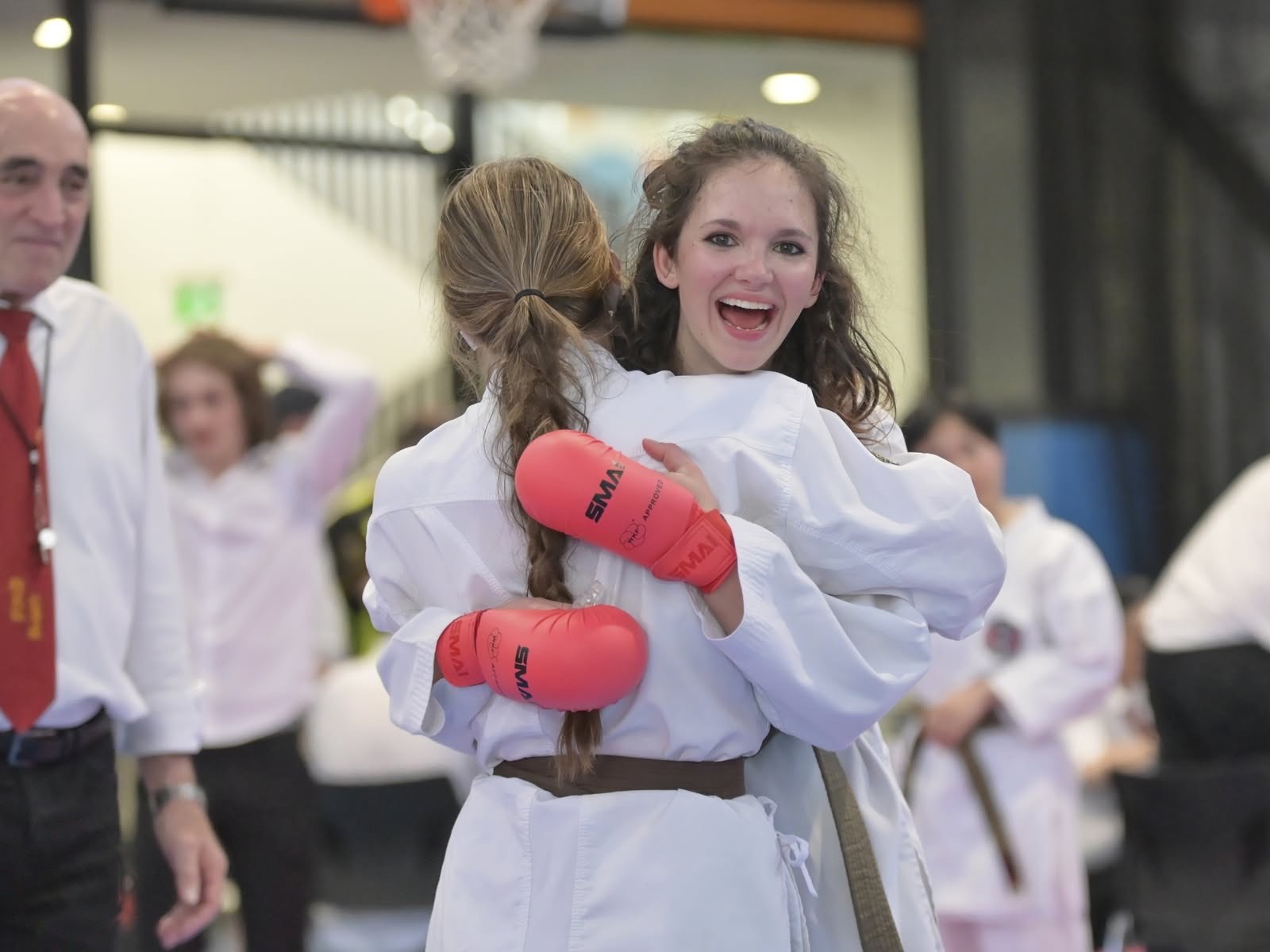 Two competitors in red gloves hugging after a bout, one beaming over the other's shoulder.